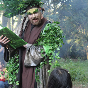 A man dressed in leaves reads from a book