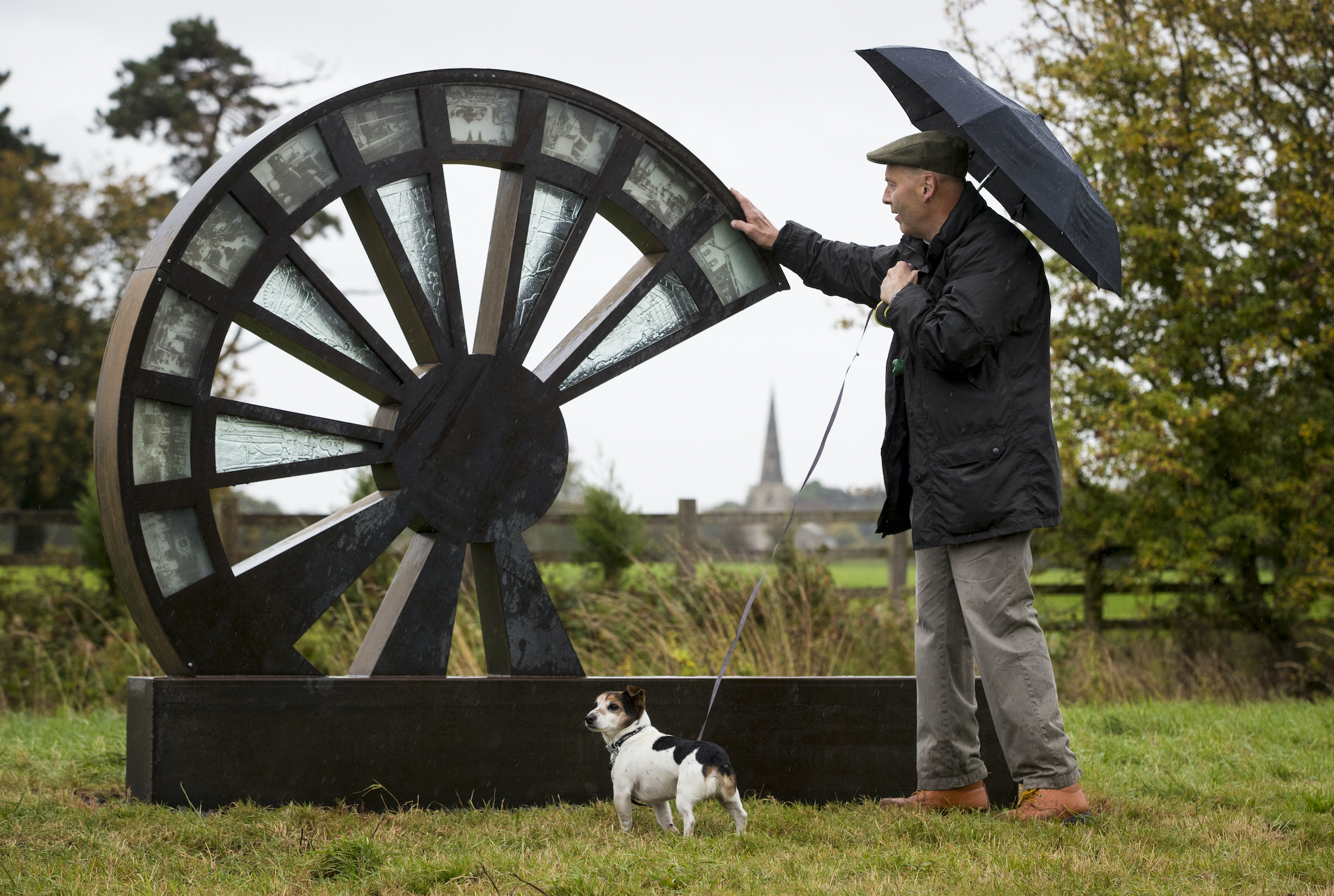 A man and his dog stand next to a wheel shaped sculpture