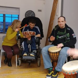 Three people sitting smiling drumming in room