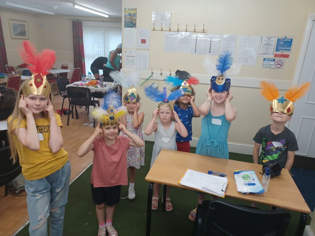 Group of children standing smiling holding festival crowns in room