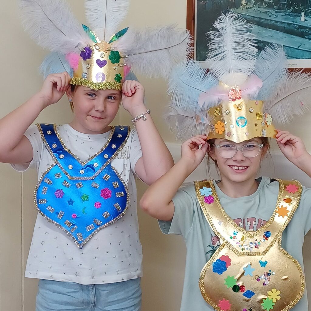 Two girls standing smiling wearing festival crowns in room