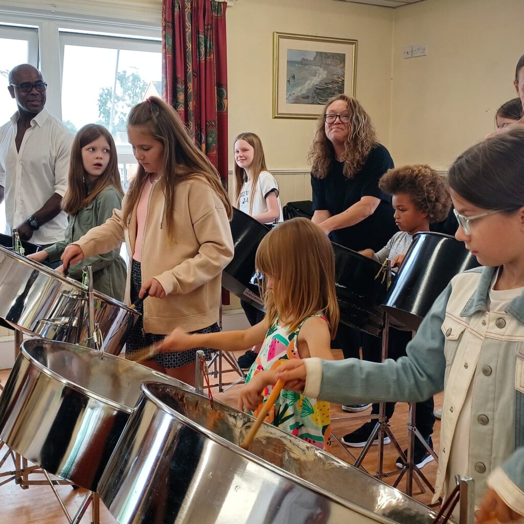 Group of people holding sticks playing big steel pan in room